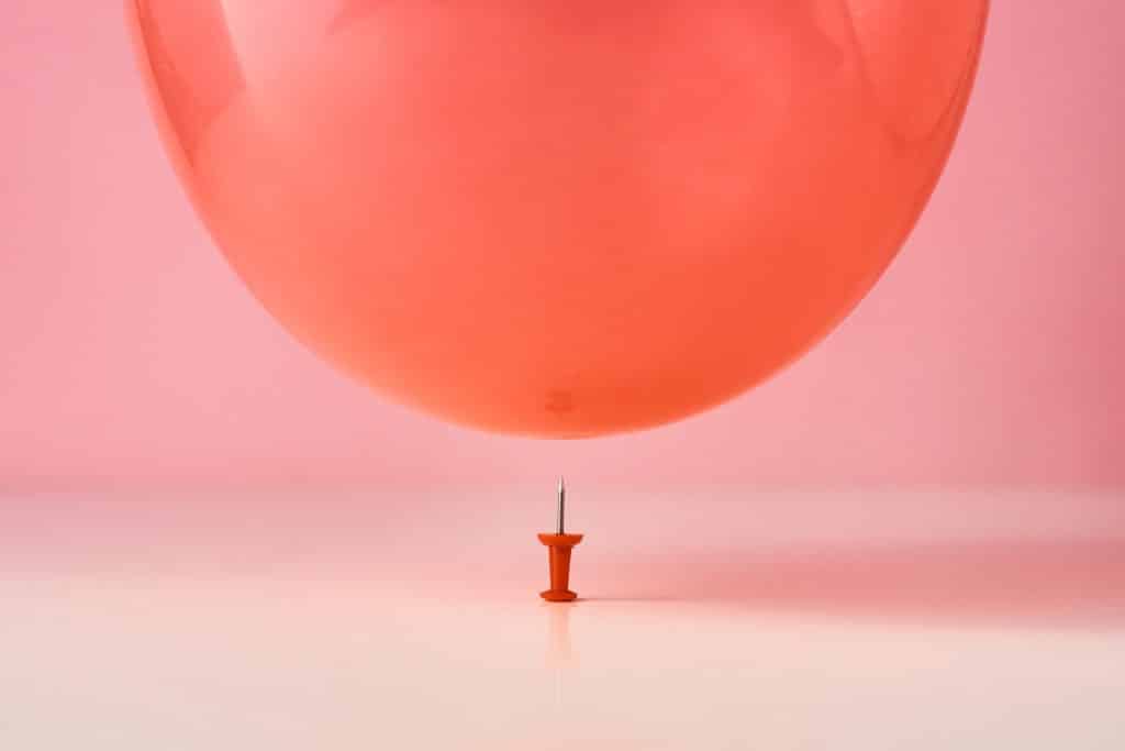 Red balloon fall on a pin needle on pink background. Danger or protection concept